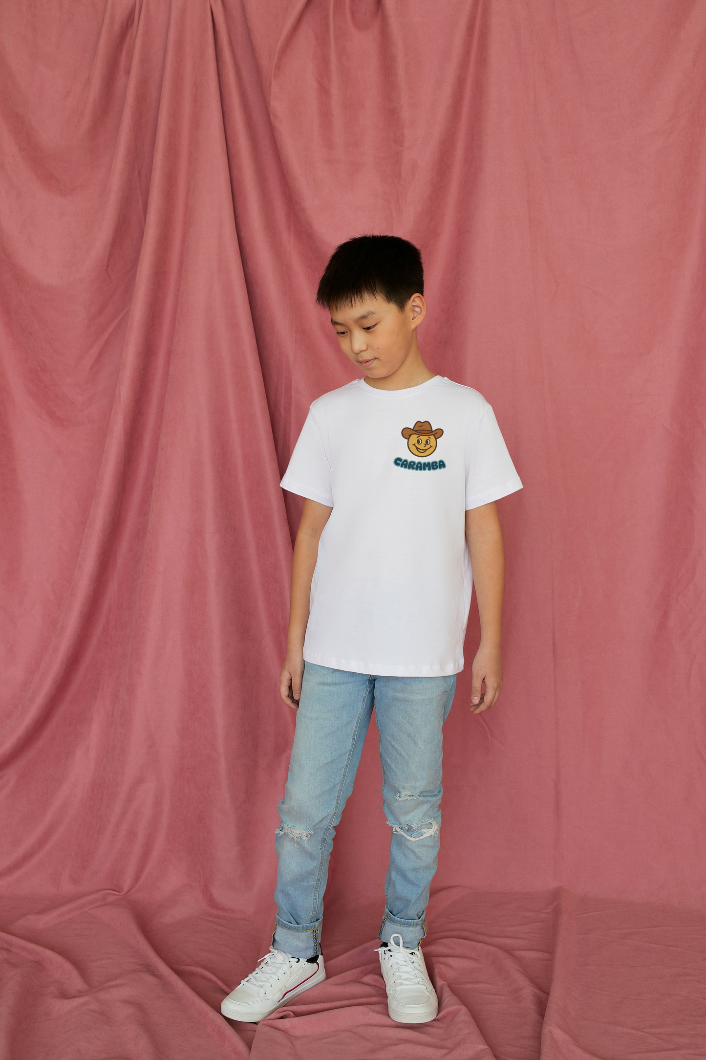 Child wearing a white t-shirt with a logo and light blue jeans against a pink curtain background