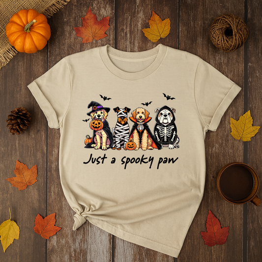 Beige t-shirt with Halloween-themed design of dogs in costumes on a wooden surface with autumn leaves and a pumpkin.